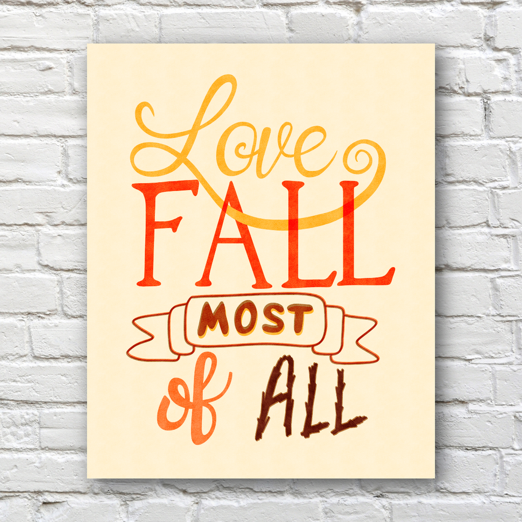 A vertical art print with the phrase 'Love FALL most of all' in warm autumn colors, displayed against a white brick wall background.