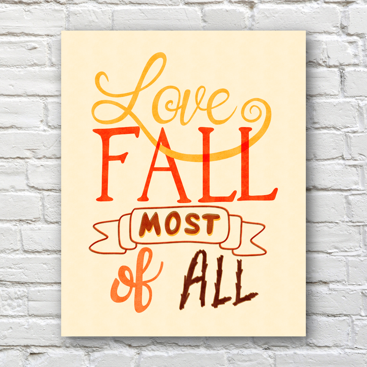 A vertical art print with the phrase 'Love FALL most of all' in warm autumn colors, displayed against a white brick wall background.