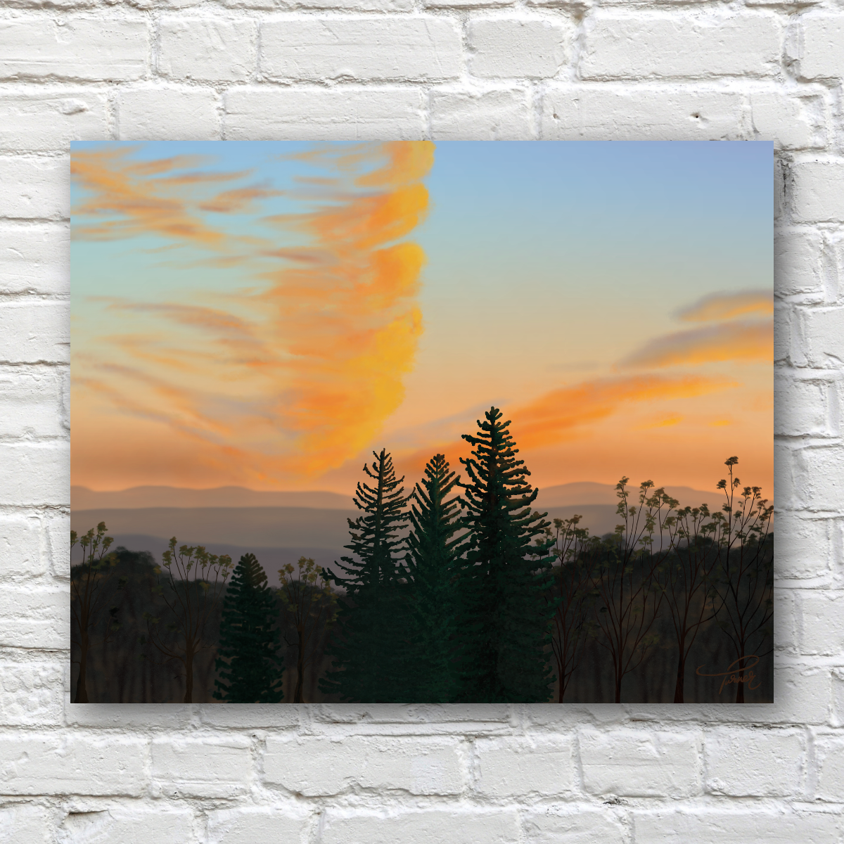 A horizontal art print showing a sunset landscape with dark evergreen tree silhouettes, distant mountains, and a sky in soft blue, peach, and orange tones, displayed against a white painted brick wall.