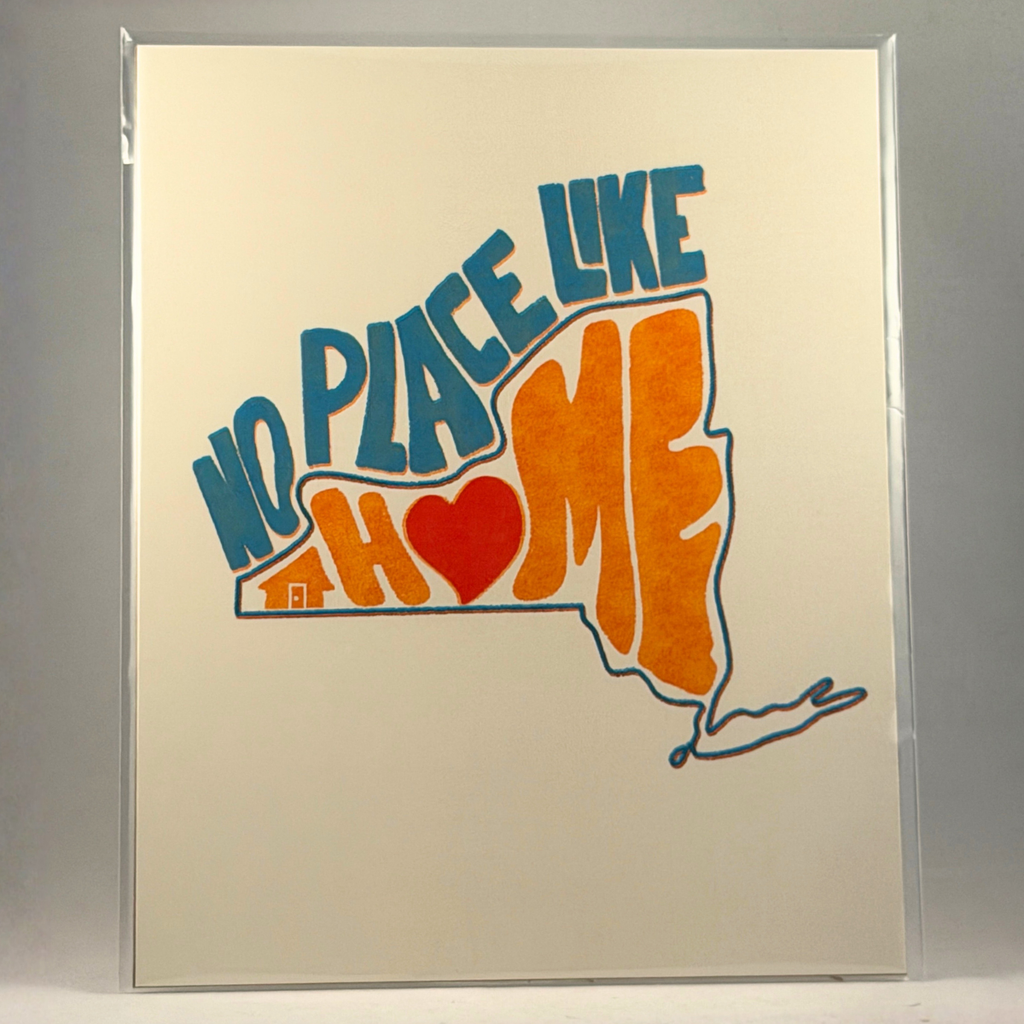 A 8x10 art print in a clear plastic sleeve, featuring the phrase 'NO PLACE LIKE HOME' in blue and orange lettering with a red heart and an orange house outline, set against a neutral gray background.