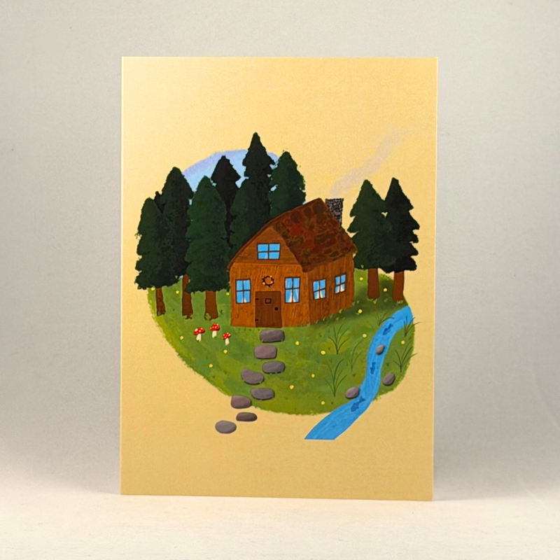 A 5x7 greeting card featuring a whimsical illustration of a small brown cabin surrounded by dark green pine trees, a winding blue stream, and a stone path, set against a warm beige background.