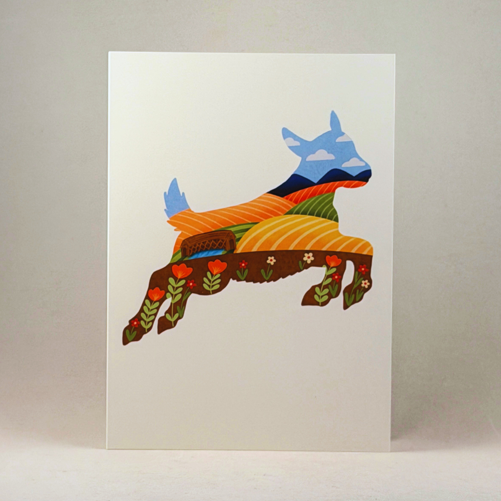 A 5x7 white art print or card featuring a stylized leaping goat filled with layered landscape and floral patterns in blue, orange, green, brown, and red, photographed against a neutral gray background.