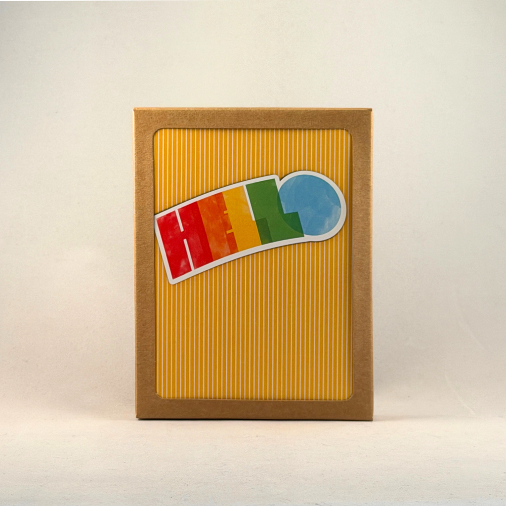A boxed notecard set with a windowed kraft brown box, featuring a yellow and white vertical striped card with the word 'HELLO' in bright rainbow colors set against the background near the top of the card. 