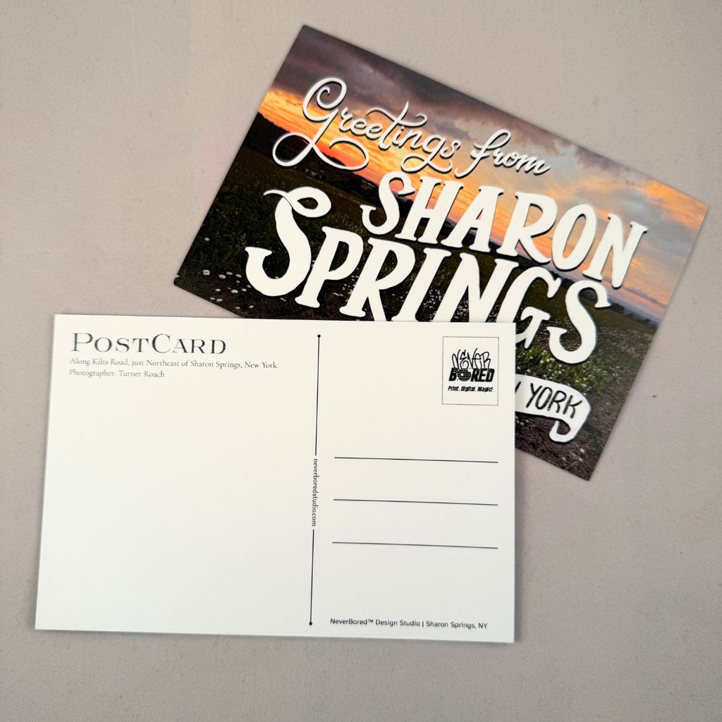 A postcard set showing the front and back on a neutral gray background. The front features a scenic sunset landscape with large white text reading 'Greetings from SHARON SPRINGS'.