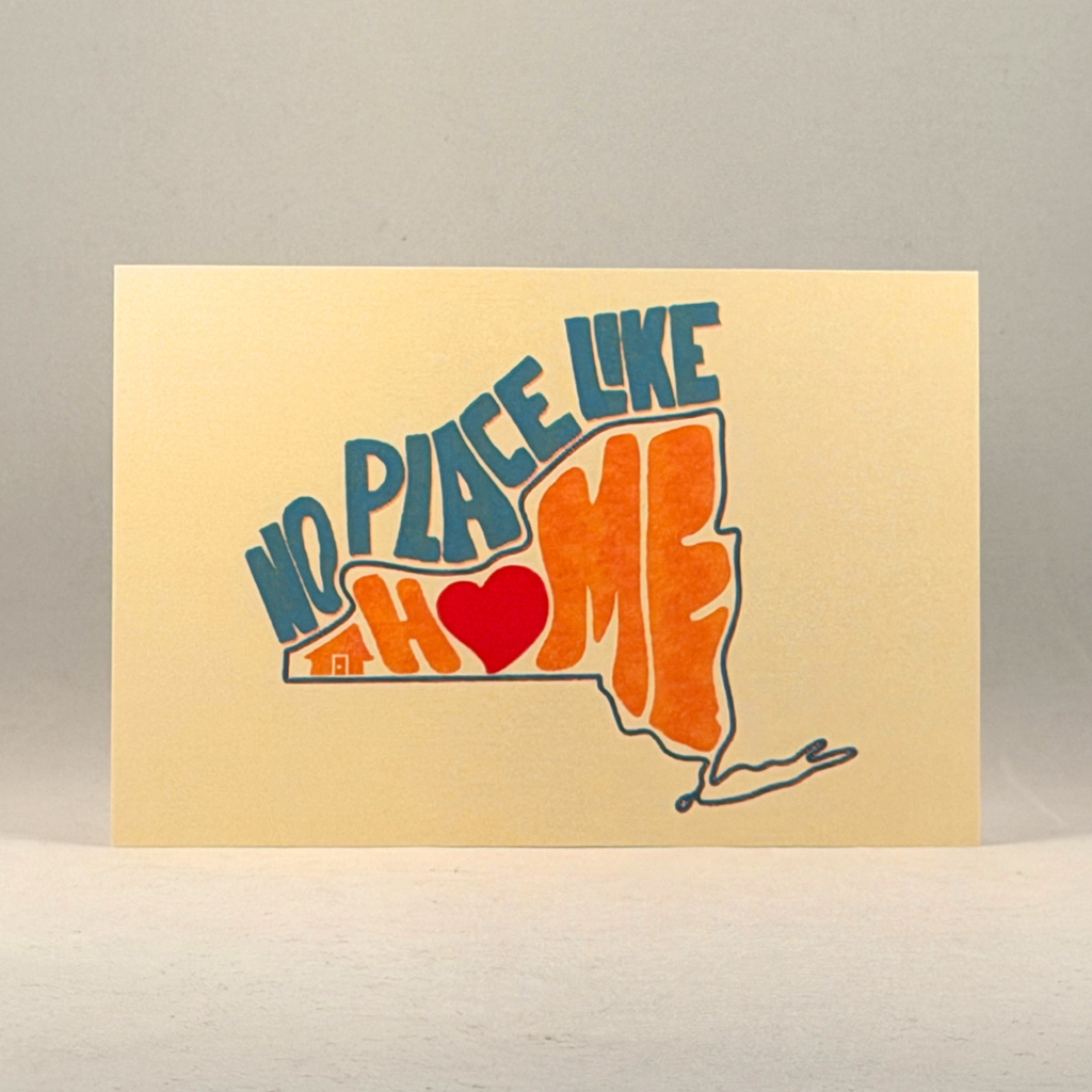 A cream-colored postcard featuring a hand-drawn style graphic of the state of New York with the text 'NO PLACE LIKE AH MY HOME' in blue and orange, with a red heart and small house details, set against a neutral gray background.
