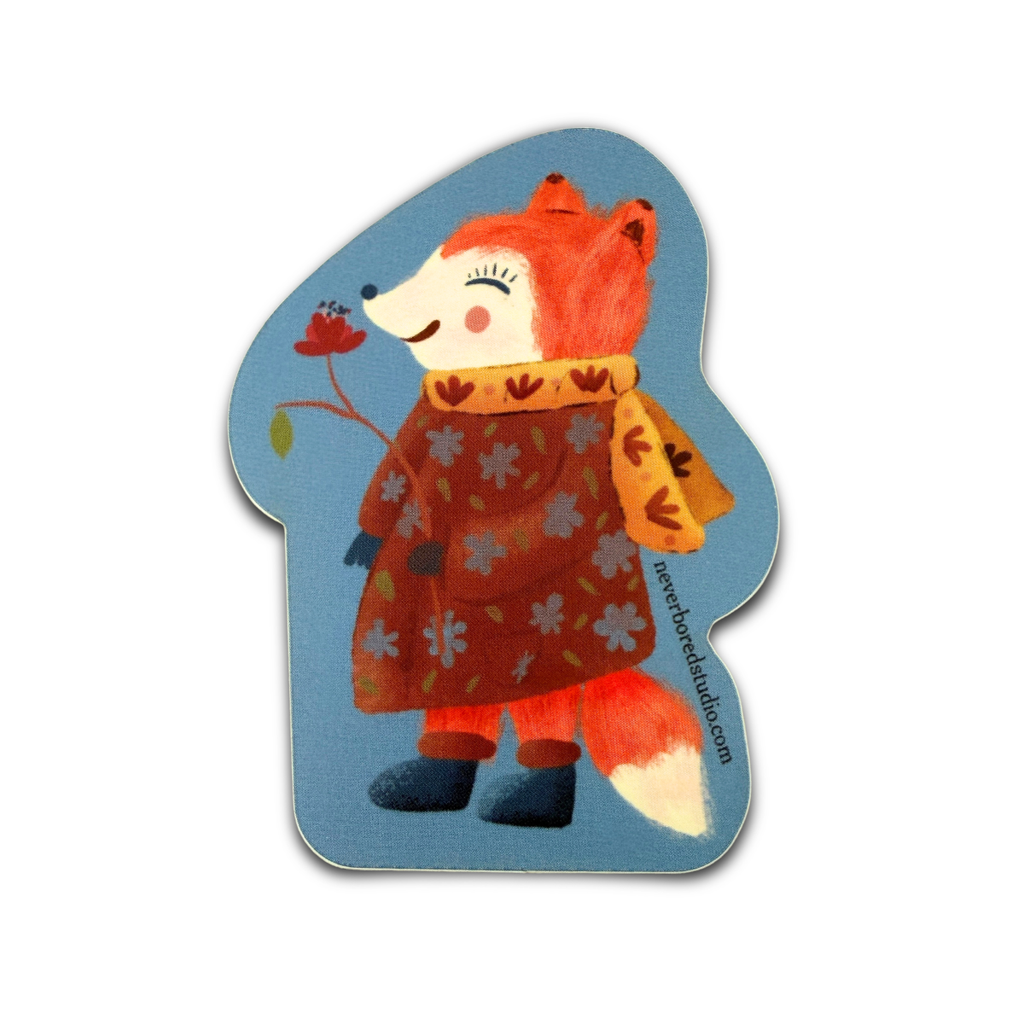 A die-cut sticker featuring a whimsical illustration of a smiling orange-red fox wearing a brown floral coat and a yellow scarf, holding a small red flower against a light blue background.