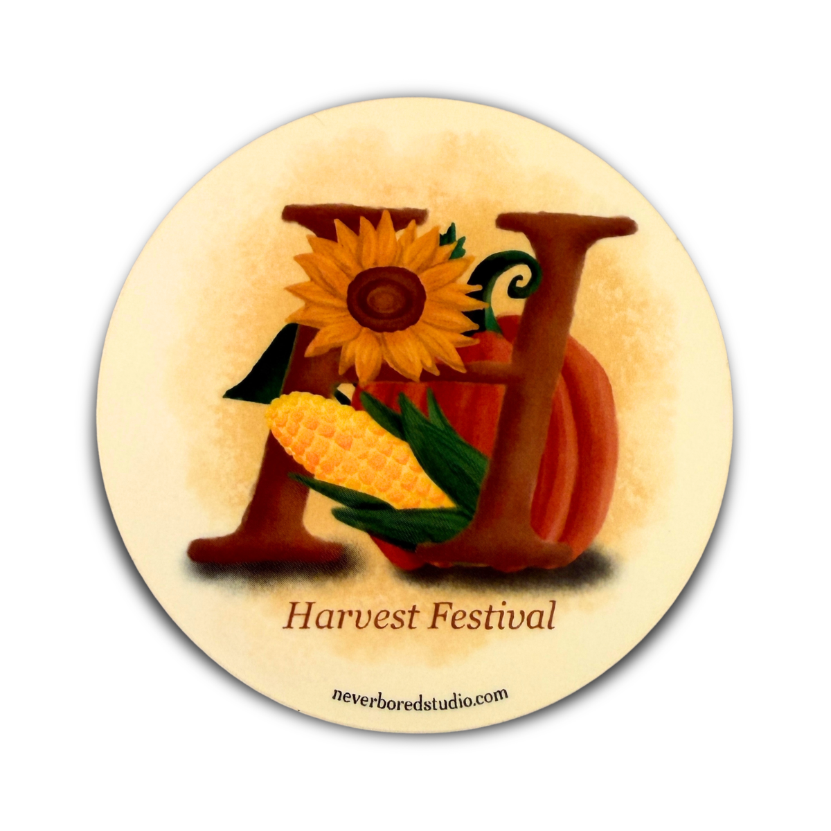 A circular autumn-themed die-cut sticker with the word 'Harvest Festival' beneath a large decorative letter H filled with a sunflower, pumpkin, and corn illustration on a cream background.