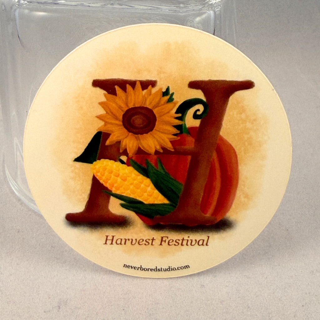 A die-cut sticker featuring a Harvest Festival design with a large letter H, a sunflower, a pumpkin, and a corn cob, shown in front of a clear glass jar.