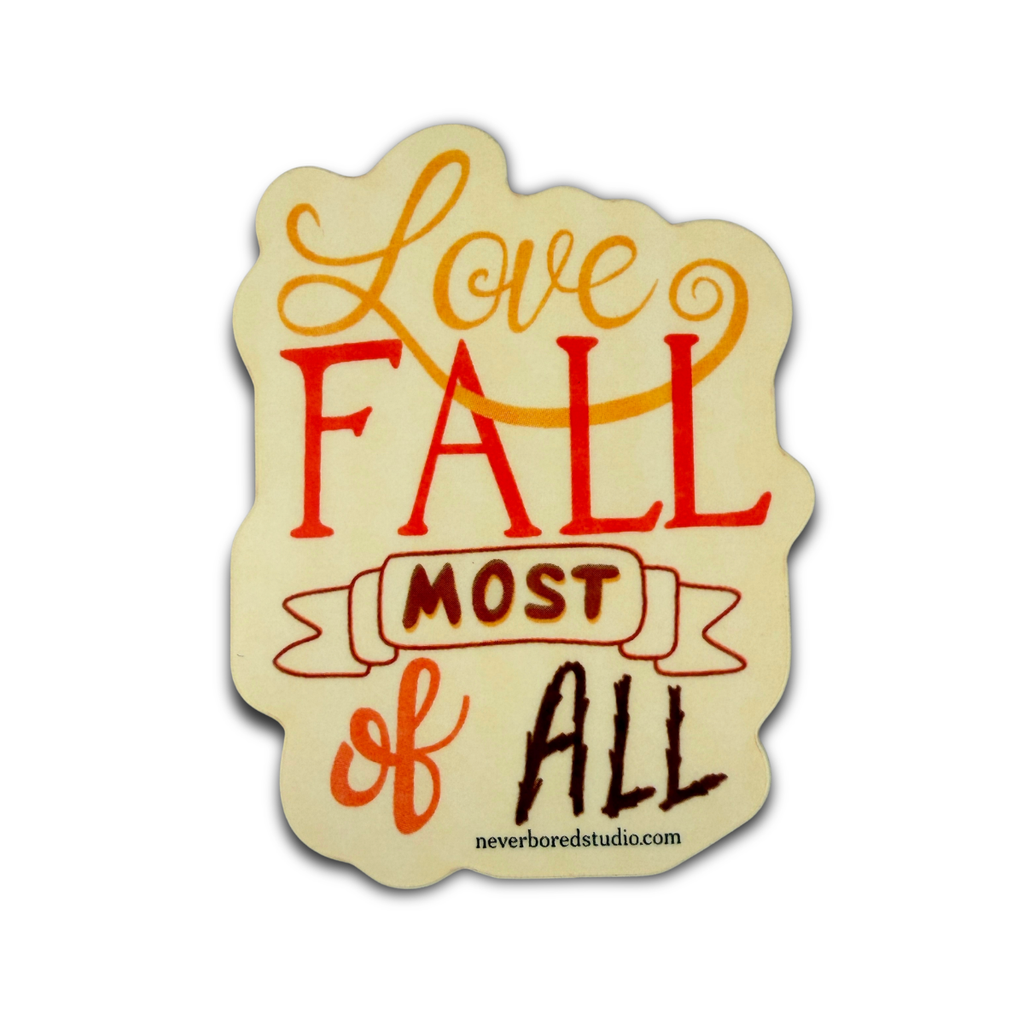 A die-cut decorative sign with the phrase 'Love FALL most of all' in stylized orange, red, and dark brown lettering on a cream background. 